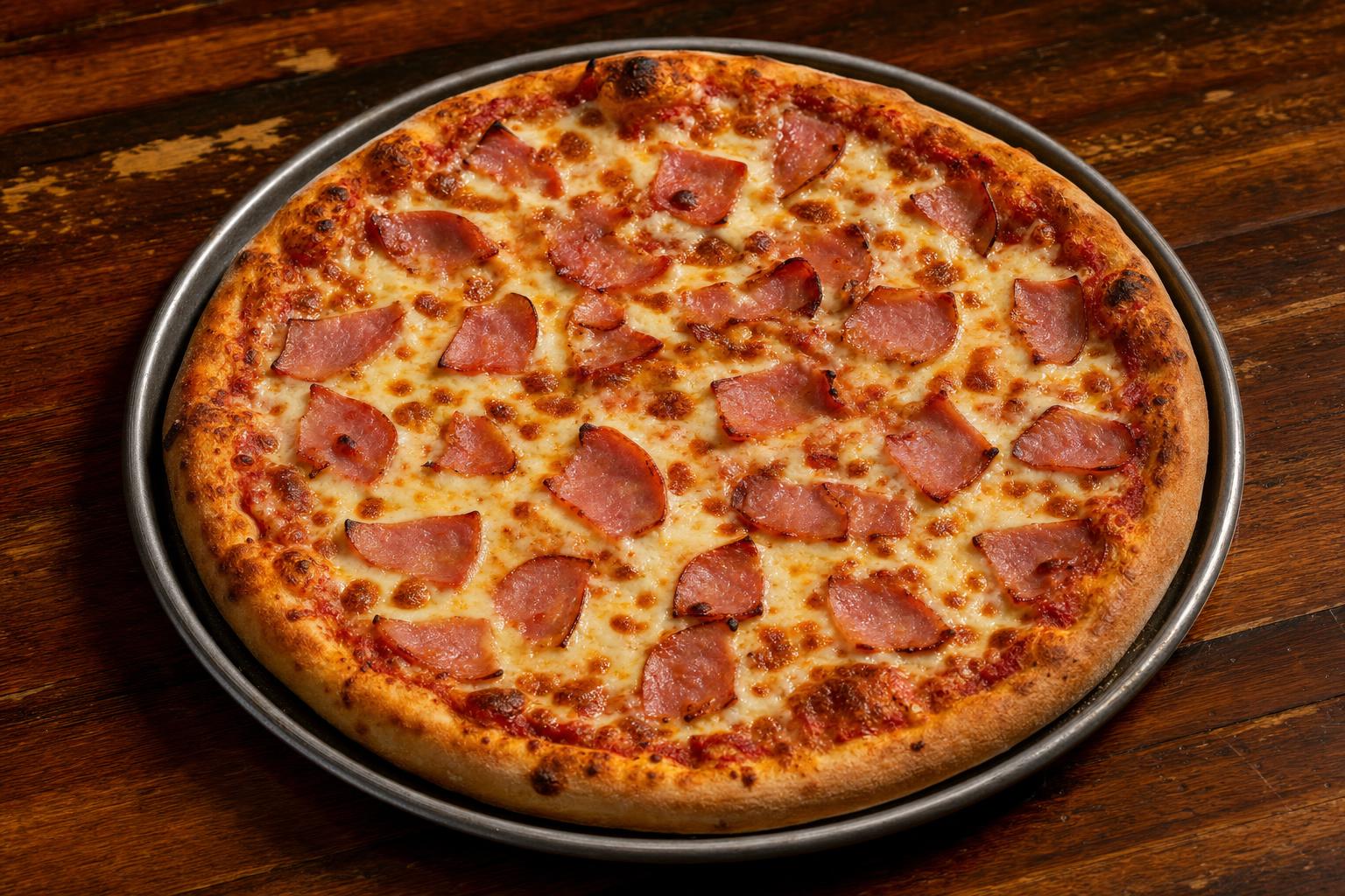 Canadian pizza with pizza sauce, mozzarella cheese, and canadian bacon on a warm wood table.