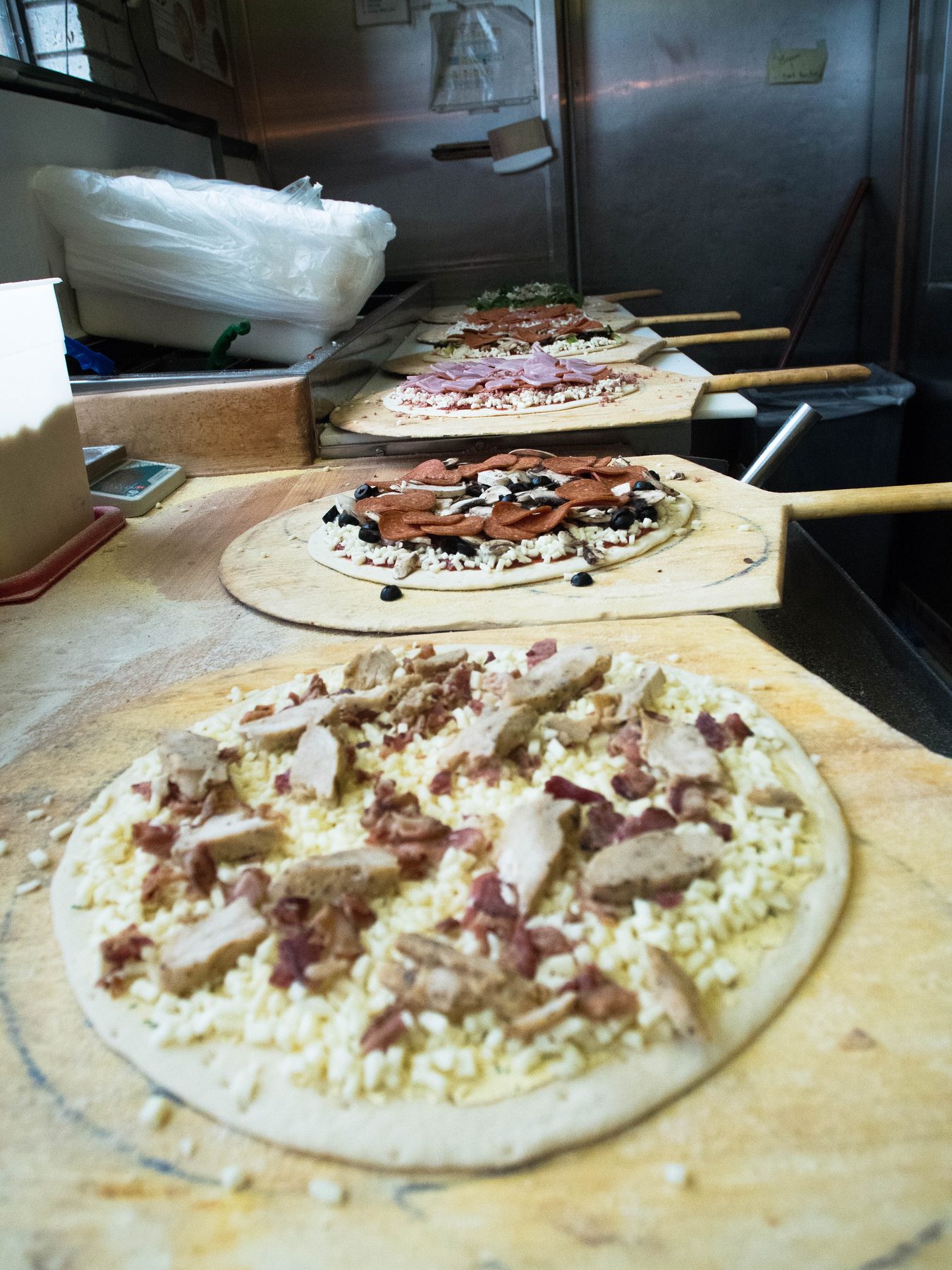 A row of topped pizzas on peels waiting for the oven