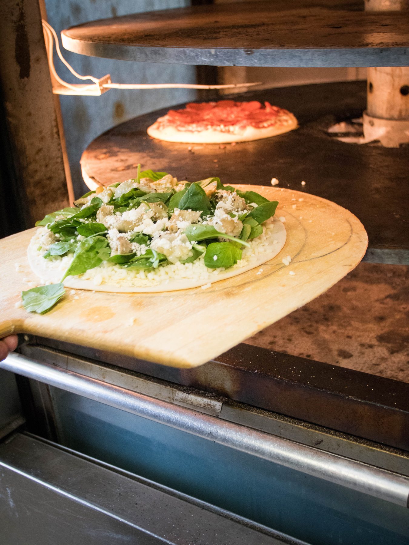 A spinach pizza going into the rotating oven