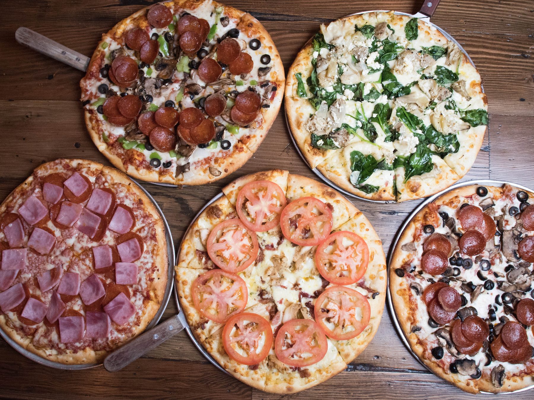 A spread of Litzas pizzas on a reclaimed-wood table