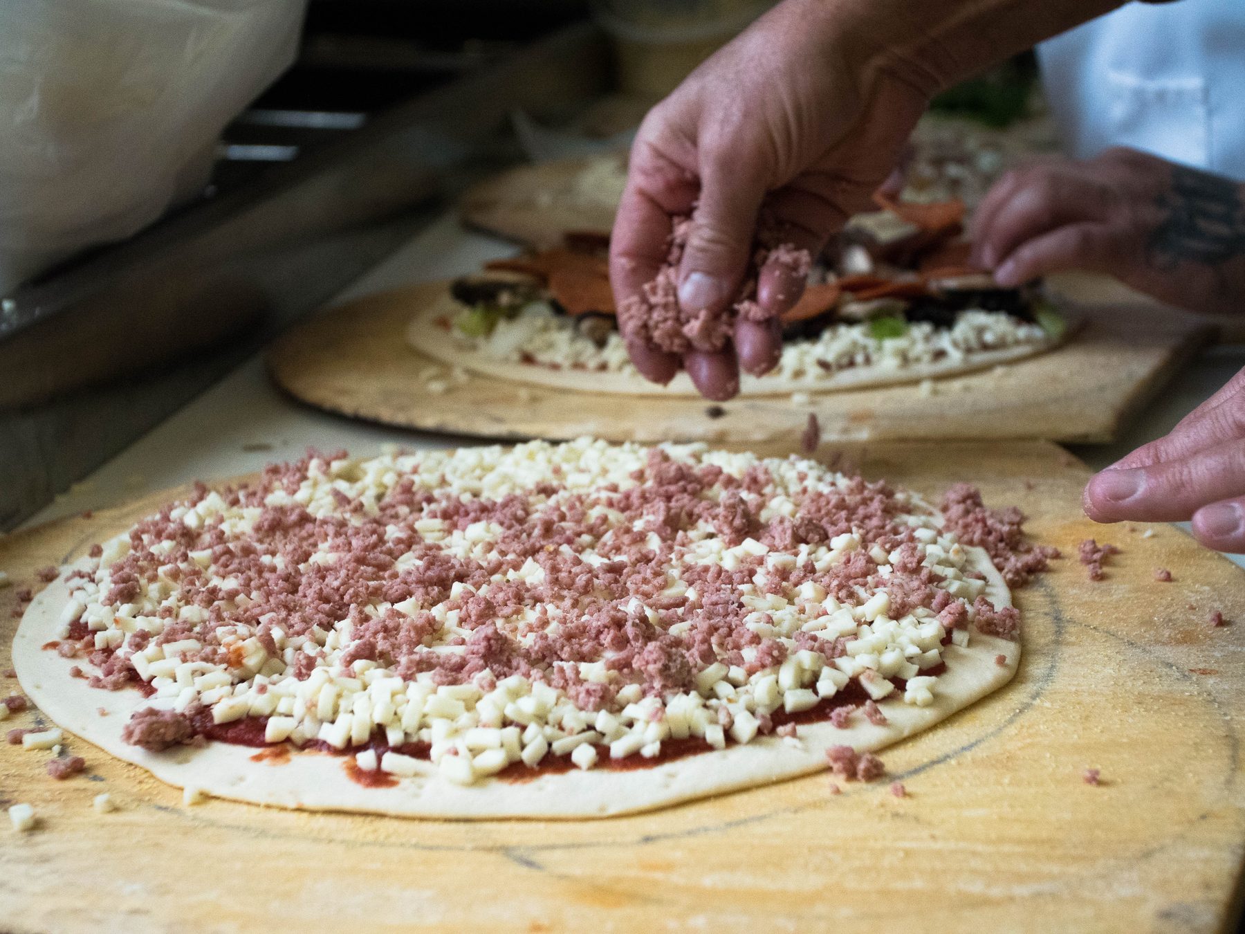 Hand-spreading sausage and cheese over fresh-rolled dough